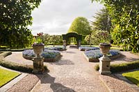 Le jardin d'été avec arcade centrale de lauel portugais et parterres de fleurs pleins de Myosotis. Holker Hall, Grange over Sands, Cumbria, Royaume-Uni.