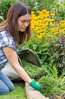 Femme répandant des boutures d'herbe autour des plantes en parterre de fleurs comme paillis