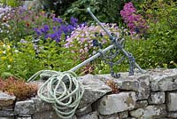 Une vieille ancre et perche de corde au sommet d'un mur en pierre naturelle à l'extérieur d'un jardin coloré en bord de mer.