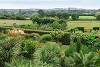 Un jardin de campagne exotique avec vue sur Hannington Hill près de Watership Down au-delà. Les plantations exotiques ci-dessous comprennent Trachycarpus fortunei, Trachycarpus wagnerianus et Musa basjoo.