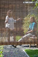 Vue des femmes discutant dans le jardin à travers un écran en osier.