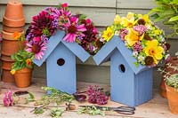 Paire de nichoirs en bois avec des toits ornés de fleurs sur un banc en bois avec des têtes de fleurs coupées et des ciseaux