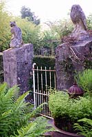 Poteaux en forme de hibou et de chat entouré de fougères luxuriantes et de clématites grimpantes à la Barn House, Glos en mai