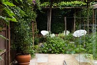 Jardin de la cour moderne avec Parrotia persica - arbres espalier en bois de fer persan - et chaises blanches modernes.