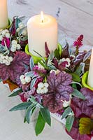 Arrangement de bougies d'automne avec Heuchera, feuilles de Buddleja, fleurs de Hebe, gousses de Lablab purpureus et Symphoricarpos - snowberry.