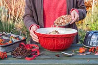 Femme ajoutant des noix et des graines au saindoux dans un bol à émail pour faire un gâteau bundt de mangeoire pour oiseaux.