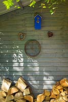 Magasin de rondins à l'arrière de la maison d'été avec nichoir, cœurs de saule tissés et vieux tamis de jardin.
