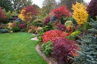 Une vue très colorée de la pelouse et des parterres densément plantés du Four Seasons Garden, un jardin à thème oriental avec des conifères, des azalées, des acers et une maison de thé.