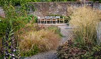 Admirez les plates-bandes mixtes de plantes vivaces et d'herbe dans le jardin contemporain jusqu'à la table et les chaises. Conception du jardin Elks-Smith.