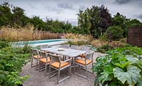 Table à manger et chaises avec vue sur la piscine, dans un jardin contemporain près de Winchester, Hants, UK. Conception du jardin Elks-Smith.