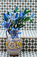 Lys coupés orientaux bleus teints dans un vase décoratif, sur fond de carreaux ornés.