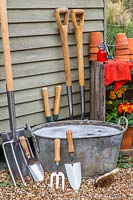 Outils de lavage: Nettoyez les outils de jardinage appuyés contre le côté de la remise à sécher à côté d'une cuve métallique d'eau savonneuse.