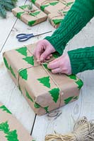 Femme attachant un noeud de chaîne sur un cadeau de Noël enveloppé avec du papier d'emballage imprimé à la main