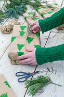 Femme ajoutant une parure d'aiguille de pin au cadeau de Noël emballé avec du papier d'emballage imprimé à la main et de la ficelle.