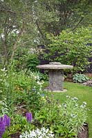 Ancienne meule utilisée comme table avec des parterres de plantes herbacées plantées, y compris Hosta, Geranium, Dactylorhiza elata - Marsh Orchid-, Centaurea, Viola blanc et Thalictrum