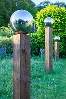 Gros plan d'un globe miroir en acier inoxydable monté sur poteau en bois, partie d'une avenue par chemin dans un pré avecCamassia subsp. leichtlinii