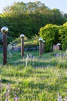 Vue sur prairie avec Camassia subsp. leichtlinii avec des ombres projetées par avenue de globes de miroir en acier inoxydable montés sur des poteaux en bois