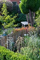 Jardin de style oriental, avec clôture en bambou, carillons éoliens, jeune Ginkgo biloba et Juniperus topiarisé.