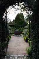 Vue à travers la passerelle en métal gothique de la pièce d'eau centrale en métal et le jardin Knot au-delà, à Abbey House Gardens, Malmesbury, Royaume-Uni.