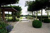 Jardin moderne, avec une zone de gravier, une pergola en bois et un plan d'eau avec des terrasses pavées.
