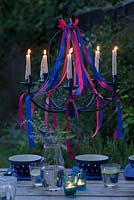 Lustre ruban avec des bougies allumées, suspendu au-dessus d'une table à manger au crépuscule.