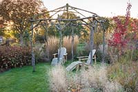 Deux fauteuils inclinables en bois sous tonnelle rustique dans un jardin respectueux de la faune avec des couleurs automnales.