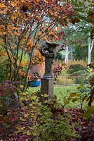 Statue en pierre posée sur un socle, nichée dans un bois au milieu des érables japonais.