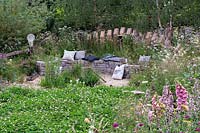Pelouse de trèfle et banc en pierre courbée dans un jardin semi-sauvage. RHS Hampton Court Festival 2019.