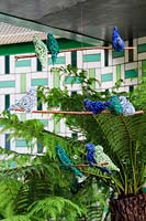 Le Jardin de bienfaisance Greenfingers. Mobile d'oiseau en fil vert et bleu avec Dicksonia Antarctica - Fougère arborescente et mur carrelé en céramique géométrique en vert et blanc derrière. Commanditaire: Greenfingers Charity