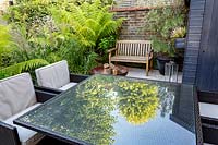 Coin salon et terrasse dans un petit jardin tolérant à l'ombre à Londres avec un thème vert. La plantation comprend Calamagrostis x acutiflora Karl Foerster, Dicksonia antarctica.