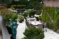 Jardin de toit urbain contemporain avec mur végétal vert de sedums tolérants à la sécheresse et Erigeron karvinskianus, table à manger et chaises sur terrasse, pots
