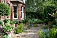 Vue sur jardin de gravier jusqu'à une ligne de Buxus - Boîte - balles en pots debout sous la baie vitrée de la maison