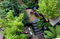 Vue sur le patio moderne dans un long jardin mince, entouré de plantations luxuriantes.