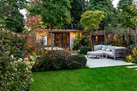 Jardin contemporain à Wandsworth montrant l'éclairage du jardin. Avec terrasse en pierre, sièges, tables et salon de jardin