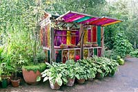 Serre colorée avec des fenêtres en verre coloré et Hostas dans des pots en face, Dalston Eastern Curve Garden, London Borough of Hackney.