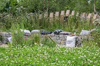 Banc en pierre sèche incurvée soutenu par une palissade en bois entourée de vivaces à fleurs - The BBC Spring Watch Garden au RHS Hampton Court Festival - Conception: Jo Thompson en consultation avec Kate Bradbury