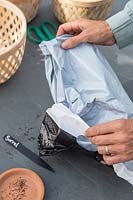 Femme transformant un sac de compost en plastique à l'envers pour couper et utiliser comme doublure