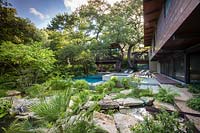 Vue sur rocaille à la piscine par maison et bois au-delà