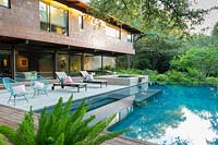 Vue sur la terrasse en bois et la piscine vers le salon extérieur et la maison contemporaine