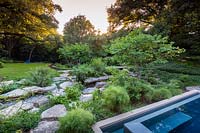 Jardin de roche calcaire entre le bord d'une piscine et un jardin boisé