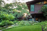 Jardin boisé aux côtés d'une maison contemporaine et pelouse incurvée avec bordure Carex
