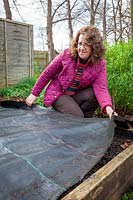 Couvrir un parterre de fleurs dans le potager avec des bâches noires pour réchauffer le sol et éviter les mauvaises herbes