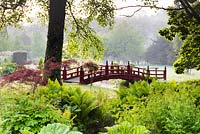 Pont Nikko rouge dans le jardin japonais en mai à Heale Garden, Wiltshire avec des ruisseaux bordés d'astilbes, Osmunda regalis, Matteuccia struthiopteris et acers au premier plan.