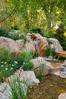 Une cascade construite à partir de gros rochers et de petits rochers, intercalée avec une variété de plantes à fleurs et à feuilles feuillues