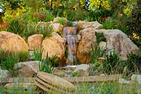 Une cascade d'aspect naturaliste faite de roches de grès rustique et plantée d'une variété d'arbustes et d'herbes
