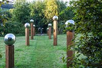 Avenue dans le pré. Globes de miroir en acier inoxydable sur des piliers en bois de hauteur irrégulière. La sculpture mobile au point focal est 'Octo' par Stuart Stockwell.Veddw House Garden, Monmouthshire, Wales, UK.