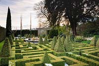 Un jardin de nœuds de Buxus écrêté - Boîte - avec des pyramides de boîtes panachées et un étang central de vannerie