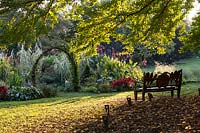 Lever du soleil au jardin Chanticleer. Banc en bois avec des détails végétaux sculptés donnant sur la cuisine et les jardins de coupe.