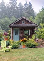 Cabane rustique dans un jardin de campagne, décorée de jardins en pot orange et de chaises Adirondack chartreuse.