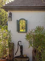 Un miroir pour reproduire une fenêtre dans un cadre vert en bois et augmente la lumière dans le jardin et ajoute de l'intérêt au mur du site. Une pompe à eau vintage dans un baril ajoute une touche d'intérêt.